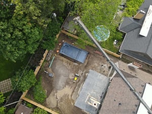 Crane setting a fiberglass swimming pool into an inground pool excavation